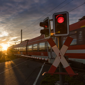 Landeseisenbahnaufsicht Ein Zug durchquert einen Bahnübergang. Der Bahnübergang ist mit einer Schranke gesichert. Vor der Schranke steht eine rote Ampel.