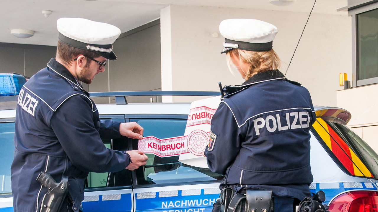 Zwei Polizisten bekleben ein Polizeiauto mit einer Werbefolie, auf der K-Einbruch steht.