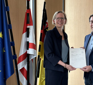 Staatssekretärin Simone Schneider übergibt dem Bürgermeister der VG Zell, Jürgen Hoffmann, den Förderbescheid.
