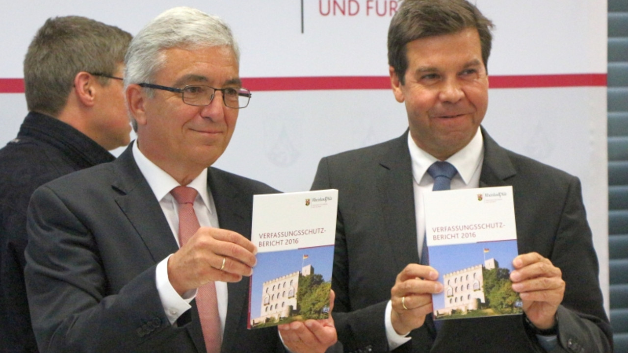 Minister Lewentz und der Leiter des Verfassungsschutzes RLP, Elmar May, halten jeweils einen Verfassungsschutzbericht in die Kamera