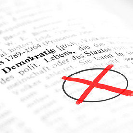 Ein rotes Wahlkreuz in einem Wörterbuch unter dem Eintrag "Demokratie"