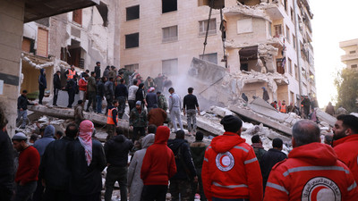 Nach dem Erdbeben der Stärke 7,8 in Syrien und der Südost-Türkei beseitigt ein Räumfahrzeug Trümmer in Hama, Syrien. Helfer vom Syrischen Arabischen Roten Halbmond unterstützen.