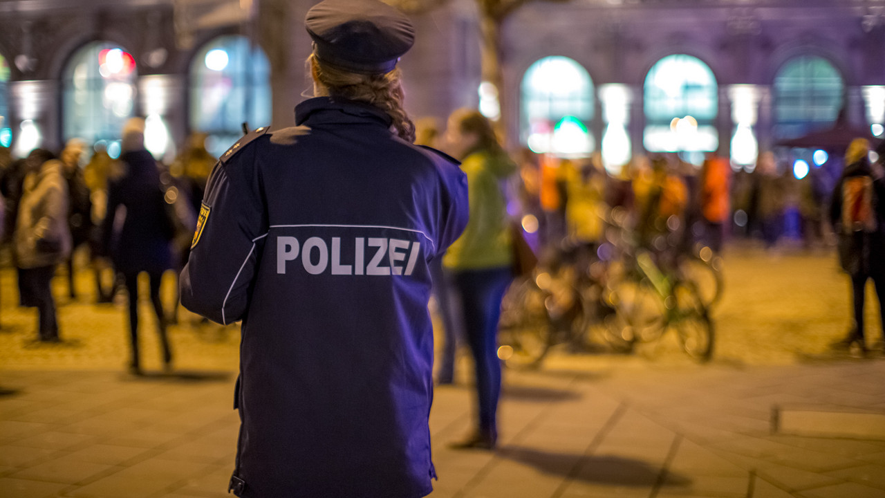 Eine Polizeibeamtin steht bei Nacht am Mainzer Hauptbahnhof. Im Hintergrund sind Menschen zu sehen.