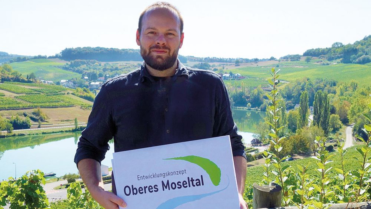 Martin Güdelhöfer, neuer Regionalmanager für grenzüberschreitende Zusammenarbeit zwischen Deutschland und Luxemburg,  hält ein Schild mit dem EOM Logo.