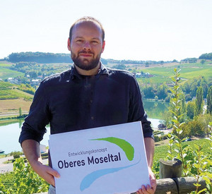 Martin Güdelhöfer, neuer Regionalmanager für grenzüberschreitende Zusammenarbeit zwischen Deutschland und Luxemburg,  hält ein Schild mit dem EOM Logo.
