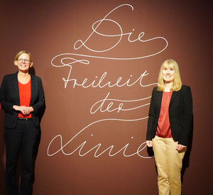 Dr. Maria Aresin, Kuratorin der Ausstellung, Innenstaatssekretärin Simone Schneider und Dr.  Birgit Heide, Direktorin des Landesmuseums, vor dem Logo der Ausstellung. 