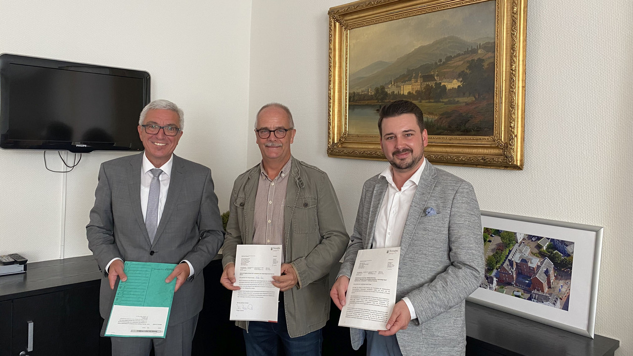 Innenminister Roger Lewentz (l.) übergibt das Aufnahmeschreiben im Beisein von Stadtbürgermeister Oliver Krügel (r.) an den VG-Beigeordneten Lutz Zaun (Mitte).