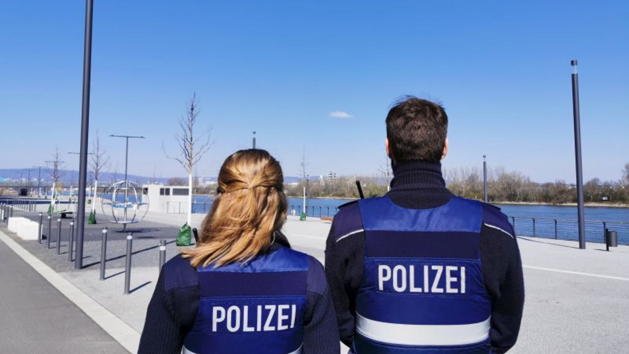 Rückenansicht einer Polizistin und eines Polizisten, die das leere Rheinufer überblicken.