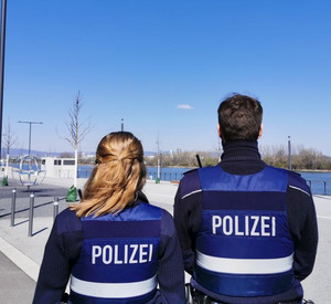 Rückenansicht einer Polizistin und eines Polizisten, die das leere Rheinufer überblicken.