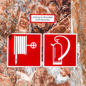 Symbole für Feuerlöscher und Löschschlauch an einer Wand