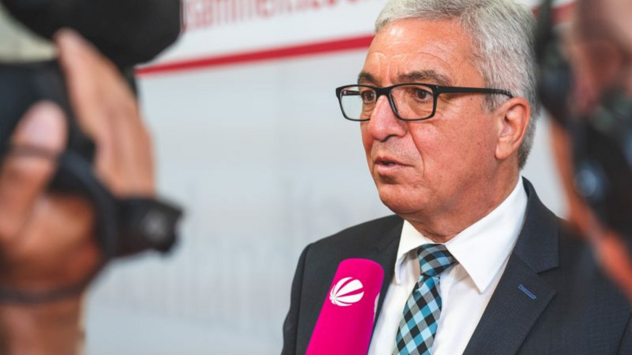 Minister Lewentz spricht in ein Mikrophon, vor ihm steht eine Kamera.