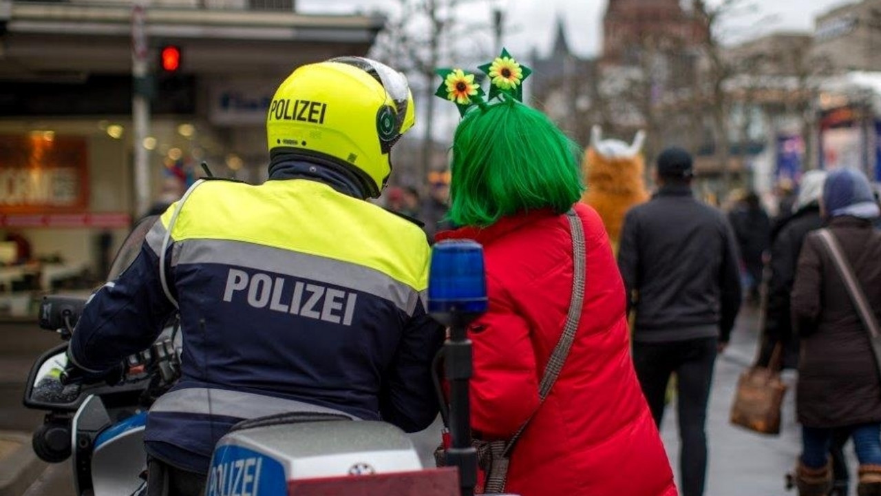 Rückenansicht einer verkleideten Frau, die einen Polizisten auf einem Motorrad etwas fragt.
