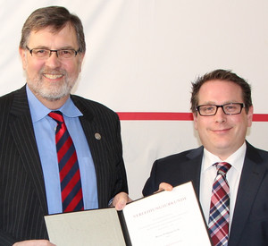 Wolfgang Groß und Ministerialdirektor Thomas Linnertz halten gemeinsam die Urkunde über die Verleihung der Ehrenurkunde in die Kamera.