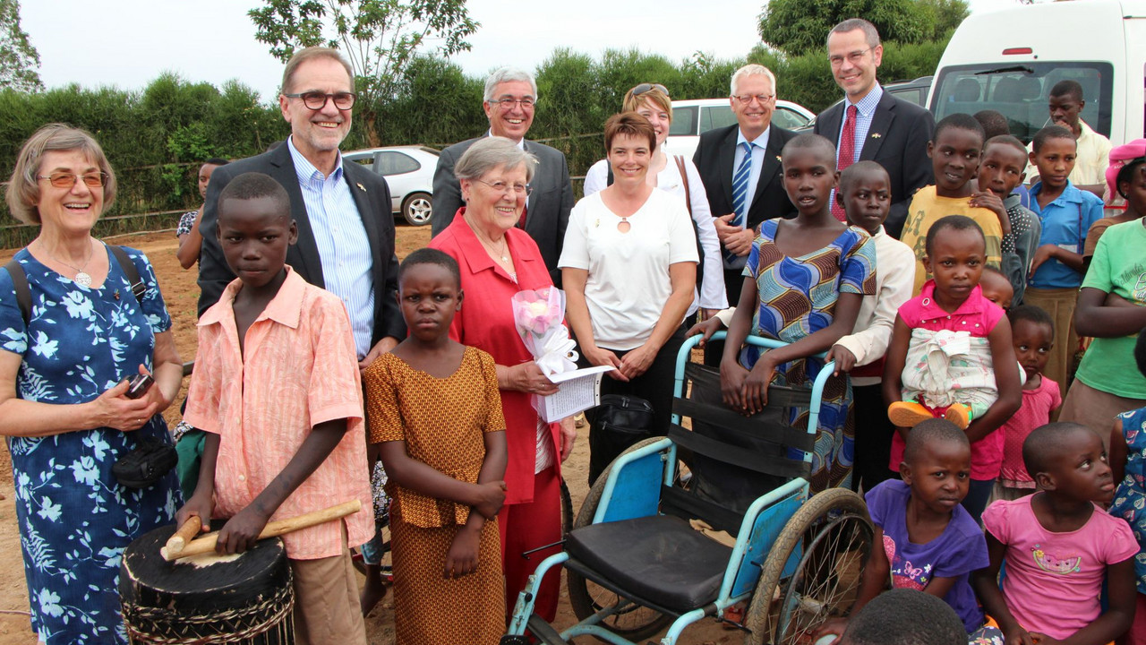 Minister Lewentz mit Mitgliedern der Delegation gemeinsam mit Kindern. In der Mitte steht ein leerer Rollstuhl.