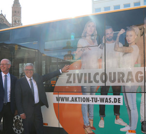 Minister Lewentz steht mit Herrn Erlhof von der Mainzer Verkerhsgesellschaft neben einem Stadtbus. Auf dem Bus prangt ein Werbebanner: Zivilcourage zeigen