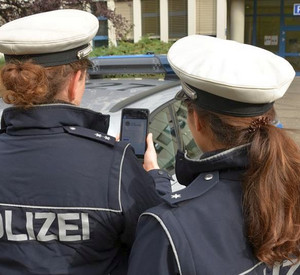Rückenansicht zweier Polizistinnen, die auf ein Handy blicken.
