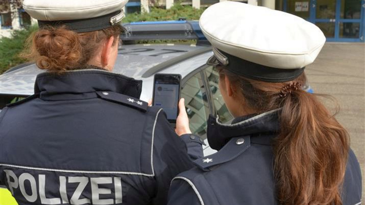 Rückenansicht zweier Polizistinnen, die auf ein Handy blicken.