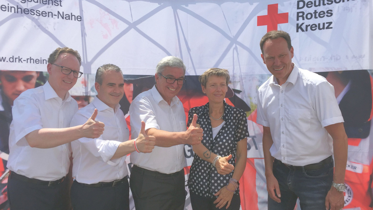 Minister Lewentz und andere stehen vor einer Stellwand des Deutschen Roten Kreuzes und strecken den Daumen nach oben.