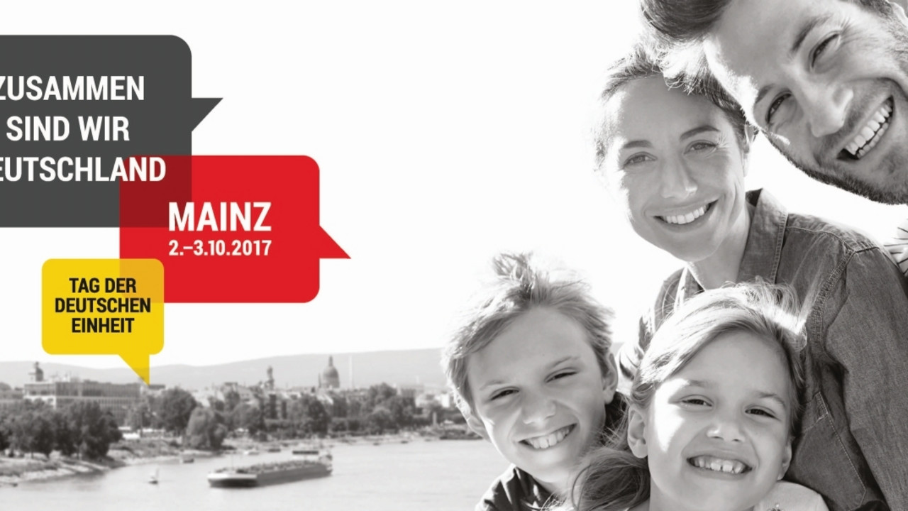 Schwarz-weiss-Selfie einer vierköpfigen Familie. Im Hintergrund ist die Stadt Mainz zu sehen. Links drei Sprechblasen in den Farben Schwarz, Rot, Gold. Jeweils in einer Blase die Texte: Zusammen sind wir Deutschland. Tag der Deutschen Einheit. Mainz 2.-3.10.2017