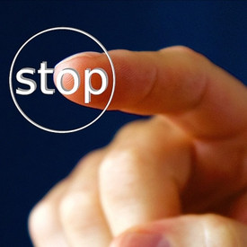 Abgebildet ist eine Hand. Der Zeigefinger drückt auf einen Knopf, auf dem Stop steht. 
