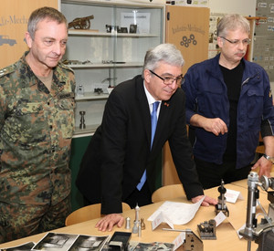 Minister Lewentz steht an einem Tisch und informiert sich in der Lehrwerkstatt der Bundeswehr in Idar-Oberstein. Links und rechts von ihm stehen Angehörige der Bundeswehr.