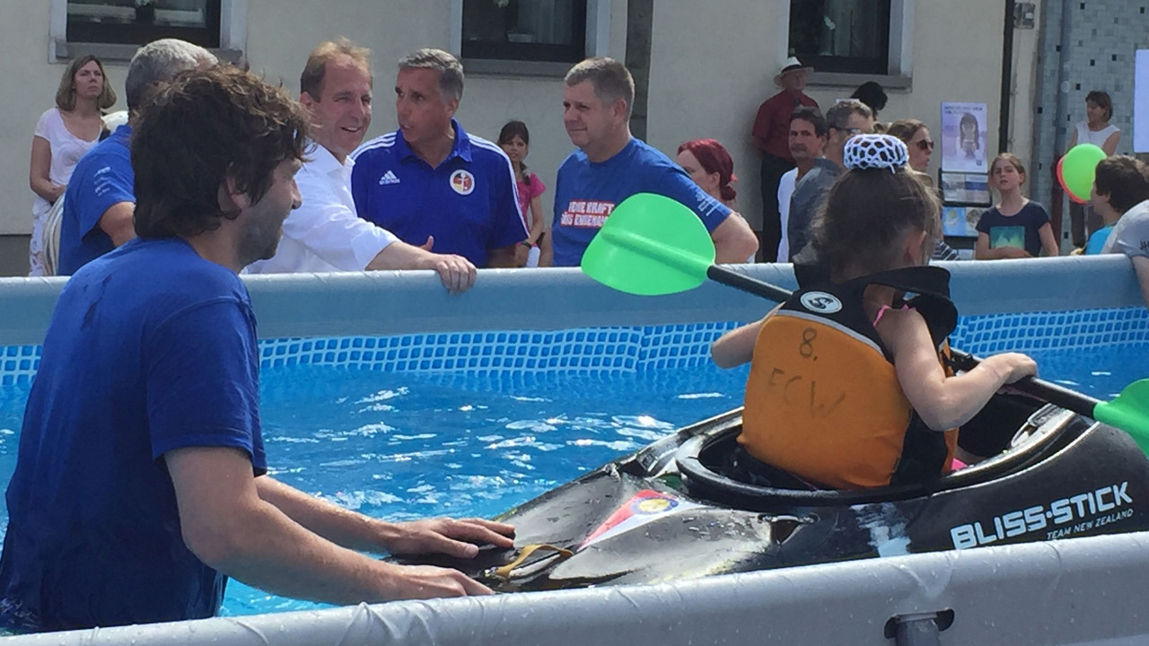 Staatssekretär Stich und andere beobachten einen Trainer, der einem kleinen Mädchen im Pool Kanufahren beibringt.