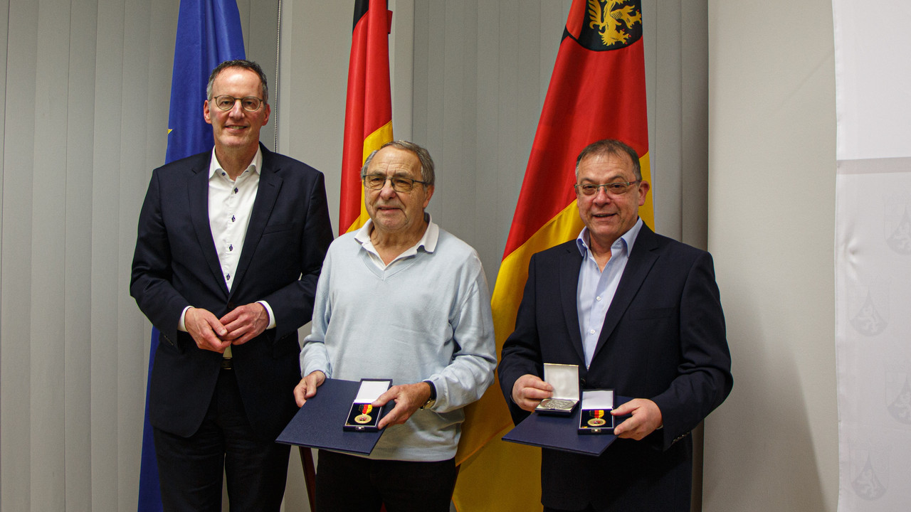 Innenminister Michael Ebling überreicht Kurt Schüller (m.) und Frederic Nageldinger (r.) die Landesverdienstmedaille.