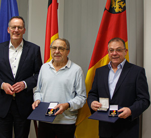 Innenminister Michael Ebling überreicht Kurt Schüller (m.) und Frederic Nageldinger (r.) die Landesverdienstmedaille.