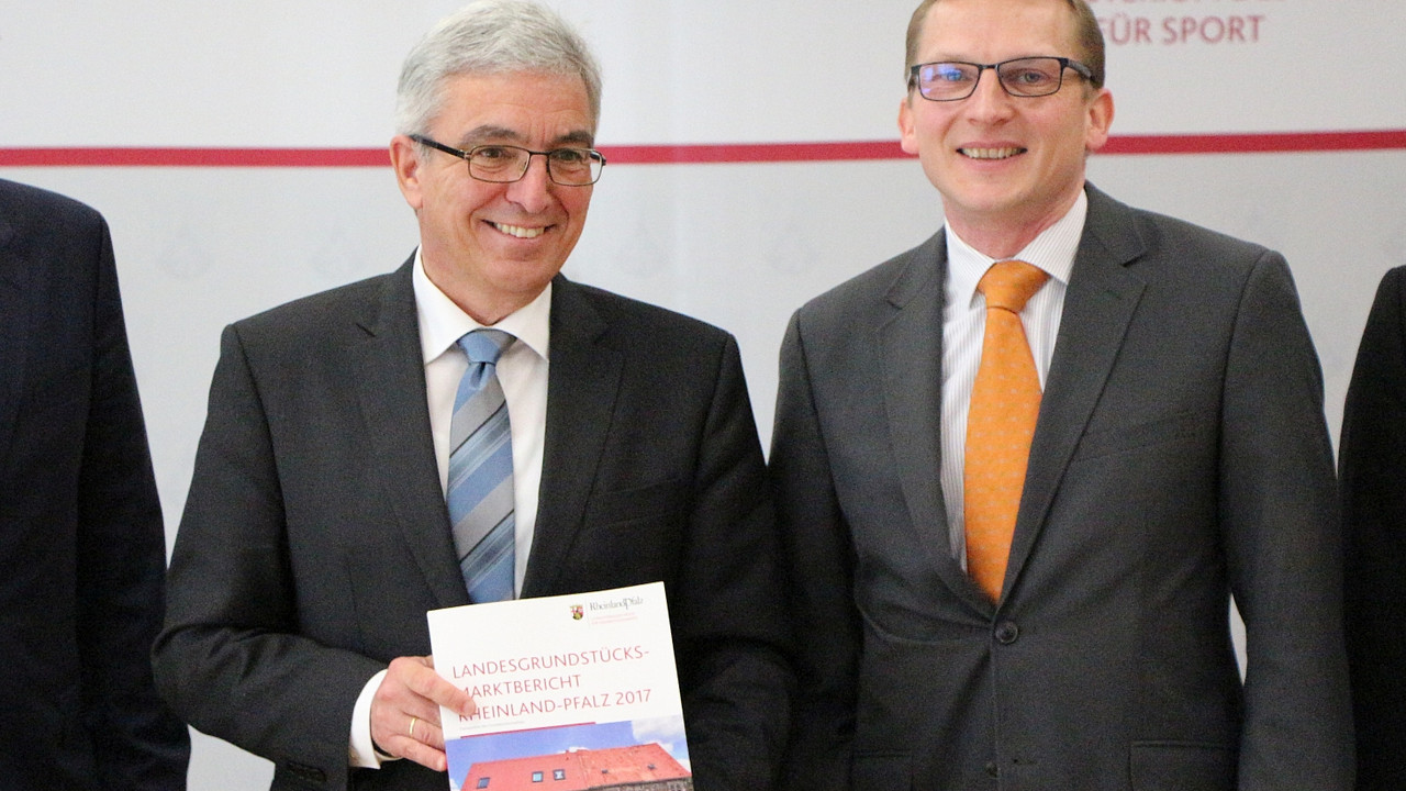 Innenminister Roger Lewentz hält den Landesgrundstücksmarktbericht 2017 in die Kamera. Neben ihm steht der stellvertretende Vorsitzender des Oberen Gutachter Ausschuss, Werner Langner